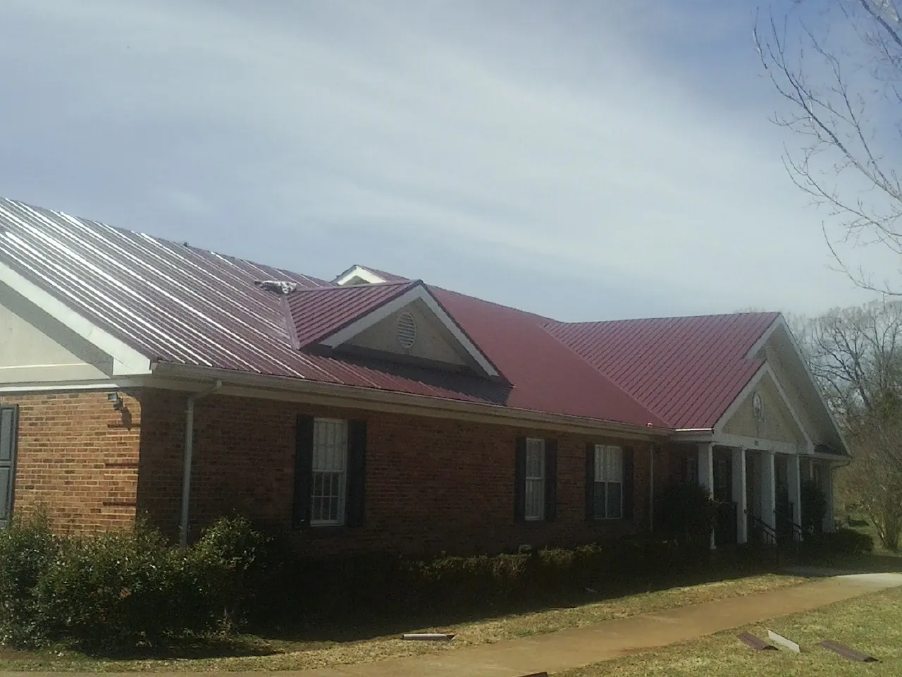 Red metal roof with gabled entries on a long brick building, from a Hail Damage Roof Repair job in Bowdon