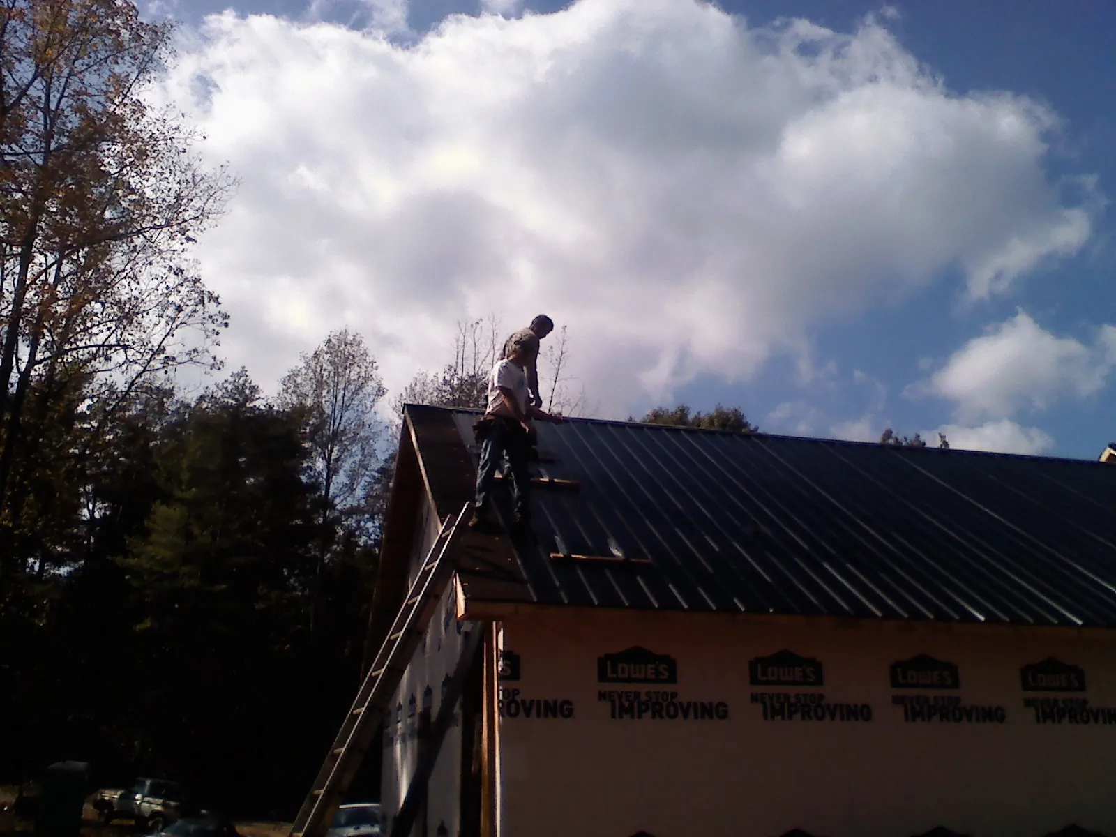 Roofer fastening dark metal panels high against a cloudy sky, from a Roof Inspection job in Bowdon