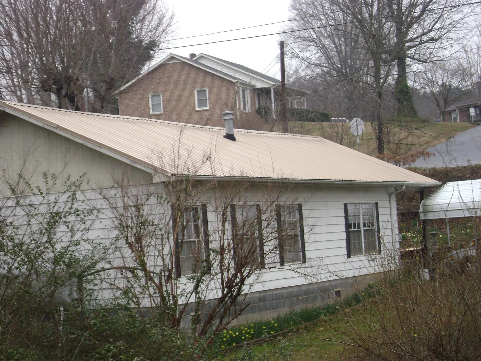 Tan metal roof on a white sided house set into a hillside — Commercial Roofing by Roofing Brothers in Bowdon