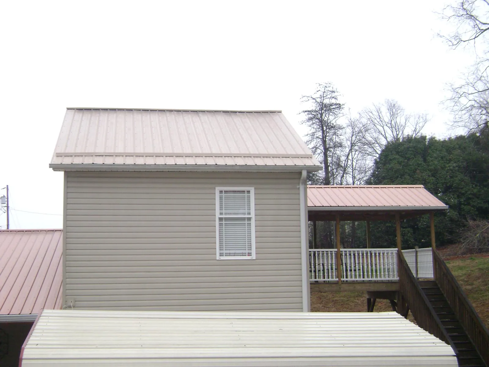 Tan metal roofs on a two story addition and attached porch, from a Roof Replacement job in Bowdon